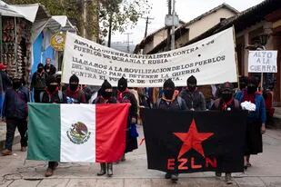 Miembros del Ejército Zapatista de Liberación Nacional sostienen una bandera mexicana y una de su movimiento durante una protesta contra el capitalismo y la guerra en Ucrania, el domingo 13 de marzo de 2022, en San Cristóbal de las Casas, estado de Chiapas, México. (AP Foto/Isabel Mateos)