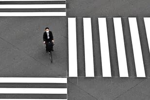 Un hombre con una máscara facial en medio de las preocupaciones por el coronavirus cruza una calle en bicicleta en Tokio el 25 de mayo de 2020