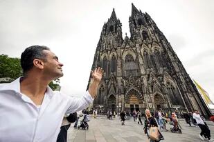 El refugiado sirio Fadel Alkhudr posa frente a la Catedral de Colonia, de la que construyó una réplica de madera de dos metros de alto y 1,40 de ancho. Foto del 20 de junio del 2022. (AP Photo/Martin Meissner)