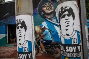 Un hincha se prepara para partir en su motocicleta junto a un mural que muestra al fallecido Diego Armando Maradona, el jueves 25 de noviembre de 2021, en Buenos Aires (AP Foto/Rodrigo Abd)