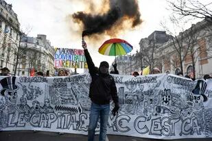 Un manifestante sostiene una bomba de humo delante de una pancarta anticapitalista durante una manifestación en un segundo día de huelgas y protestas en todo el país por la reforma de las pensiones propuesta por el gobierno, en París el 31 de enero de 2023