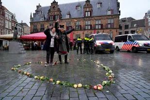 Dos mujeres posan luego de colocar unas rosas en forma de corazón mientras la policía vigila el centro de la ciudad de Nimega, Holanda, luego de que se prohibió la realización de una protesta contra las restricciones de COVID-19, el domingo 28 de noviembre de 2021. (AP Foto/Peter Dejong)