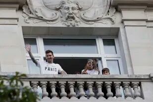 El futbolista argentino Lionel Messi saluda a sus seguidores desde el balcón de su hotel mientras su esposa, Antonella Roccuzzo, toma fotografías, en París, el 10 de agosto de 2021. (AP Foto/Adrienne Surprenant)