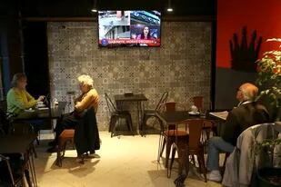 La gente mira por televisión las renuncias de los ministros en un bar en Mar del Plata