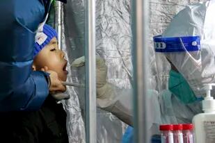 En esta foto publicada por la agencia de noticias Xinhua, personal de salud toma una muestra bucal a un niño para una prueba de COVID-19 en una zona residencial del distrito de Fengtai, Beijing, el domingo 23 de enero de 2022. (Tang Rufeng/Xinhua via AP)