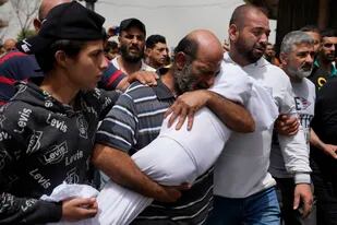 Un hombre llora mientras carga el cuerpo de una niña durante el funeral de siete personas que murieron cuando un bote abarrotado de migrantes se hundió el fin de semana cuando la Armada libanesa trató de obligarlo a regresar a la costa, en Trípoli, en el norte de Líbano, el lunes 25 de abril de 2022. (AP Foto/Hassan Ammar)