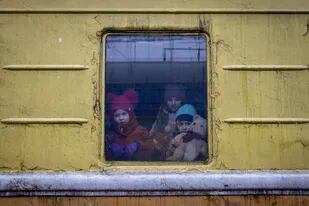 3 niños miran desde la ventana de un tren de carga utilizado para evacuar gente, en la estación de trenes de Kiev, Ucrania.