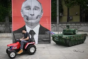Un miembro de la ONG romaní "ARESEL" arrastra con un tractor una maqueta de tanque ruso junto a un retrato del presidente ruso Vladimir Putin, durante una protesta frente a la embajada rusa en Bucarest, el 16 de mayo de 2022.