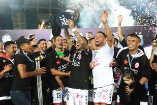 Iván Tapia acaba de recibir la copa de manos del presidente de la B Nacional, y festeja el ascenso a primera de Barracas Central