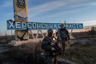 Dos miembros de las fuerzas de defensa ucranianas están parados junto a un letrero que dice "región Kherson" en las afueras de Kherson, sur de Ucrania, el lunes 14 de noviembre de 2022.