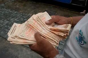 Un hombre cuenta bolívares por el valor de un dólar en una parada de autobús en Caracas (AP Photo/Ariana Cubillos,File)