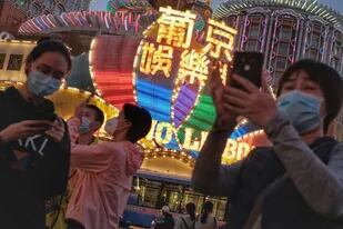 Turistas con cubrebocas tomando fotografías afuera del Casino Lisboa en Macao, China