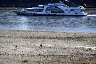 Un barco navega frente a un área seca a orillas del río Rin; se espera que los niveles de agua disminuyan aún más en los próximos días. Federico Gambarini/dpa