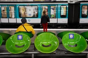Las calcomanías que dicen para "nuestra salud, deje este asiento libre", se muestran en los asientos mientras los pasajeros esperan el metro en la plataforma, en París, el 29 de abril de 2020, el día 44 de un estricto encierro en Francia para detener la propagación del coronavirus