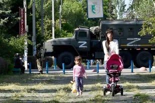 Una mujer y un niño caminan por un parque mientras los militares rusos patrullan la calle en Skadovsk, óblast de Kherson