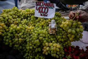 Una estatua de Buda descansa sobre uvas a la venta por un vendedor ambulante en el centro de Santiago de Chile, el 5 de abril de 2022. (AP Foto/Esteban Felix)