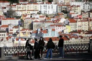 Jóvenes con mascarillas conversan en un mirador sobre el centro histórico de Lisboa