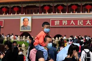 Un hombre con su hijo en los hombros fotografiado frente a un retrato de Mao Zedong en la Plaza de Tiananmen, en Beijing