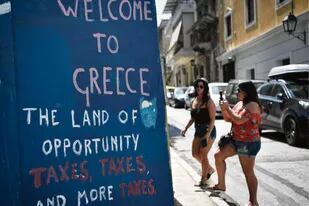 Una irónica pintada en el centro de Atenas da la bienvenida a los turistas recordándoles el exceso de impuestos vigentes