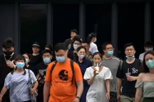 Transeúntes con mascarillas cruzan una intersección en Beijing el 6 de agosto del 2022. Unos 80.000 turistas estaban varados en el balneario chino de Sanya luego que las autoridades lo declararon un foco de COVID-19 e impusieron un encierro. (AP Foto/Mark Schiefelbein)