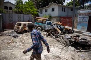 Un hombre camina frente a autos quemados en el vecindario de La Plaine, en Puerto Príncipe, Haití, el viernes 6 de mayo de 2022. (AP Foto/Odelyn Joseph)