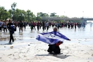Un migrante muestra una bandera de Honduras mientras cruza el Río Suchiate, desde Guatemala hacia México