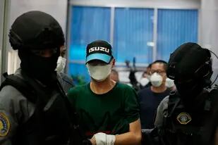 Policías tailandeses escoltan al exagente Thitisan Utthanaphon, apodado "Jo Ferrari", al salir de la División de Supresión del Delito en Bangkok, Tailandia, 26 de agosto de 2021. El excoronel y cinco subordinados fueron condenados el miércoles 8 de junio de 2022 a prisión perpetua por la tortura y asesinato de un sospechoso al que intentaron extorsionar. (AP Foto/Sakchai Lalit,File)