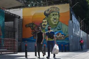 Personas con mascarillas pasan junto a un mural de Hugo Chávez y Nicolás maduro en el centro de Caracas el 28 de julio de 2020, después de que el gobierno intensificó un bloqueo nacional como medida preventiva contra la propagación del coronavirus