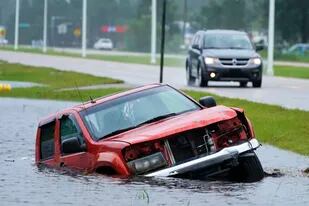 Un vehículo abandonado se ve medio sumergido en una cuneta junto a una autopista casi inundada, bajo los aguaceros del huracán Ida el domingo 29 de agosto de 2021, en Bay Sain Louis, Mississippi. (AP Foto/Steve Helber)