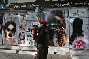 Un combatiente talibán pasa frente a un salón de belleza de Kabul con imágenes de mujeres desfiguradas con pintura en aeroso
