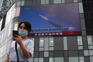 Una mujer utiliza su teléfono móvil mientras camina frente a una pantalla grande que muestra un noticiero sobre los ejercicios militares de China que rodean a Taiwán, en Pekín el 4 de agosto de 2022.