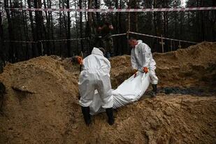 Dos técnicos forenses llevan una bolsa para cadáveres en un bosque en las afueras de Izium, en el este de Ucrania, el 16 de septiembre de 2022.