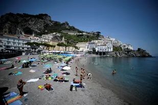 La fotografía, tomada el 2 de julio de 2020, muestra a turistas y residentes tomando sol y nadando en una playa de Amalfi en el sur de Italia