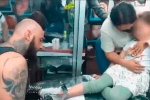 Una imagen muestra cómo la mujer intenta contener a la niña mientras el tatuador continúa con su trabjo