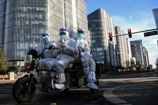 Trabajadores con equipos de protección individual (EPI) monitorean una calle de Pekín el 26 de noviembre de 2022.