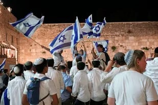 Miembros de movimientos juveniles judíos bailan y ondean banderas israelíes la víspera del Día de Jerusalén, un feriado para celebrar la toma de la zona antigua de Jerusalén en la Guerra de Oriente Medio de 1967, cerca del Muro de las Lamentaciones, el lugar más sagrado donde pueden orar los judíos, en Jerusalén, el sábado 28 de mayo de 2022. (AP Foto/Tsafrir Abayov)