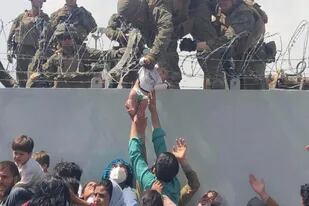 Un marine norteamericano sostiene ayer un bebé que le alcanzan los padres en el aeropuerto de Kabul