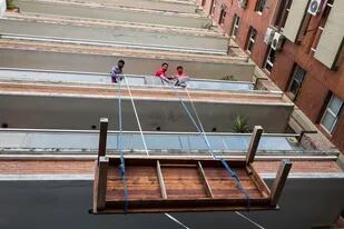 Tres empleados descargan una mesa a través de un balcón, cada uno con su barbijo
