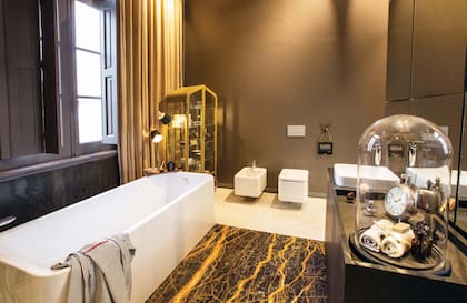 Alejandra Mahiques y Teresa Falcone son las autoras de “Baño principal”, de marcada impronta masculina. La bañadera, de corte rectangular y moderno, está acompañada por un mueble Cabinet restaurado (Baardo) y detrás de él se desploman cortinas Tusor teñidas a mano (Hilo).