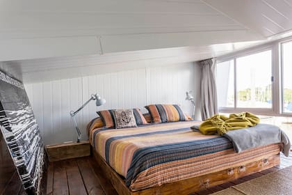 La base de la cama se recubrió en madera rústica, que continúa en las mesas de luz. Apoyadas, dos lámparas móviles.