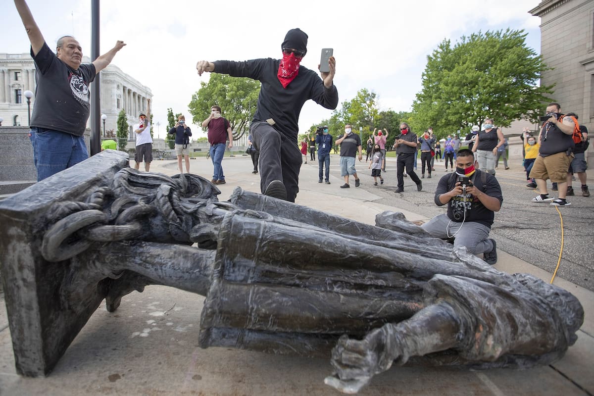 10 de junio de 2020, EE. UU., Saint Paul: un hombre patea la estatua de Cristóbal Colón que se encuentra en el suelo después de ser derribado por activistas nativos americanos en el Estado de Minnesota