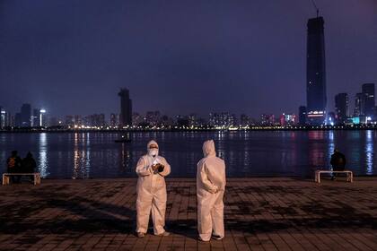 Dos personas con trajes protectores mientras visitan Hankou Beach Park en Wuhan, en la provincia central de Hubei, en China