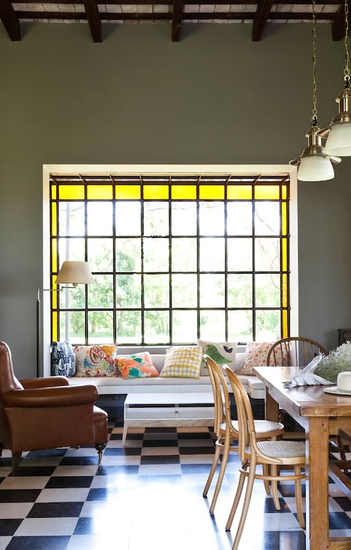 Igual que en living, el ventanal del comedor tiene vidrio repartido con guarda amarilla que suaviza la entrada de luz. Mesa con base de cobre y tapa de mármol y una taza gigantesca que se usa como florero.