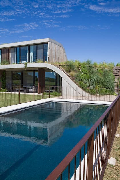 Frente a una cancha de polo, una casa con curvas, estanque interior y terrazas verdes en todos los niveles