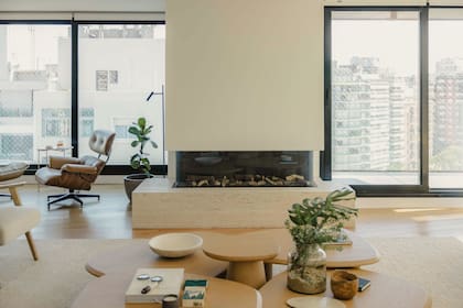 A la izquierda, el clásico sillón Eames (Más Infinito) marca el comienzo del espacio de lectura que la dueña de casa disfruta con vistas a la rambla. Al centro, la chimenea que incorporó Saravia al proyecto. “La revestimos en travertino para que se vea delicada y sutil”.