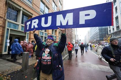 A man holds a "TRUMP" sign as people wait to get inside Capital One Arena for a rally for President-elect Donald Trump ahead of the 60th Presidential Inauguration, Sunday, Jan. 19, 2025, in Washington. (AP Photo/Mike Stewart)