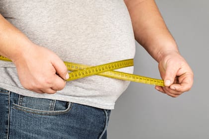 A man measures his fat belly with a measuring tape. on a gray background