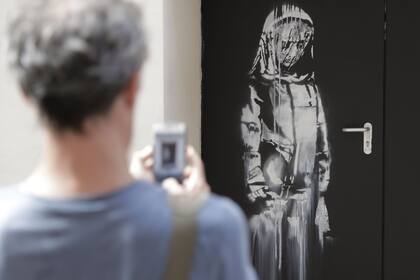 A man takes a photograph of a recent artwork by street artist Banksy in Paris on June 25, 2018, on a side street to the Bataclan concert hall where a terrorist attack killed 90 people on Novembre 13, 2015. The mysterious British street artist has created a series of new murals in Paris in the last f