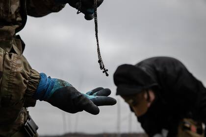 Un soldado encuentra un crucifijo mientras los trabajadores recogen los cuerpos de los soldados rusos en la región de Kharkiv, Ucrania, el 20 de enero de 2024. Los civiles que recogen a los soldados rusos muertos enfrentan muchos de los peligros de la guerra a lo largo del frente