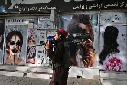 A Taliban fighter walks past a beauty saloon with images of women defaced using a spray paint in Shar-e-Naw in Kabul on August 18, 2021. (Photo by Wakil KOHSAR / AFP